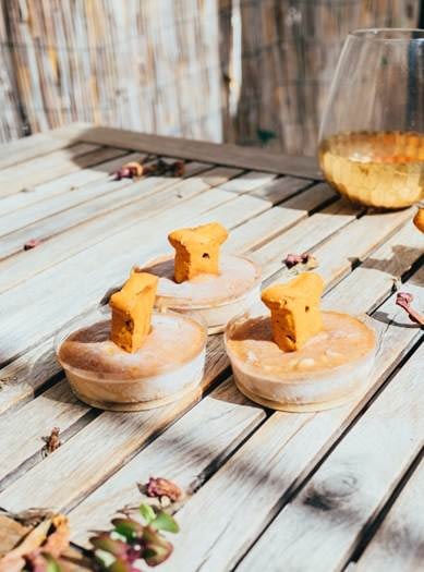 A Dog Treat Each Attached to Three Baked Cakes Placed On An Outdoor Wooden Table
